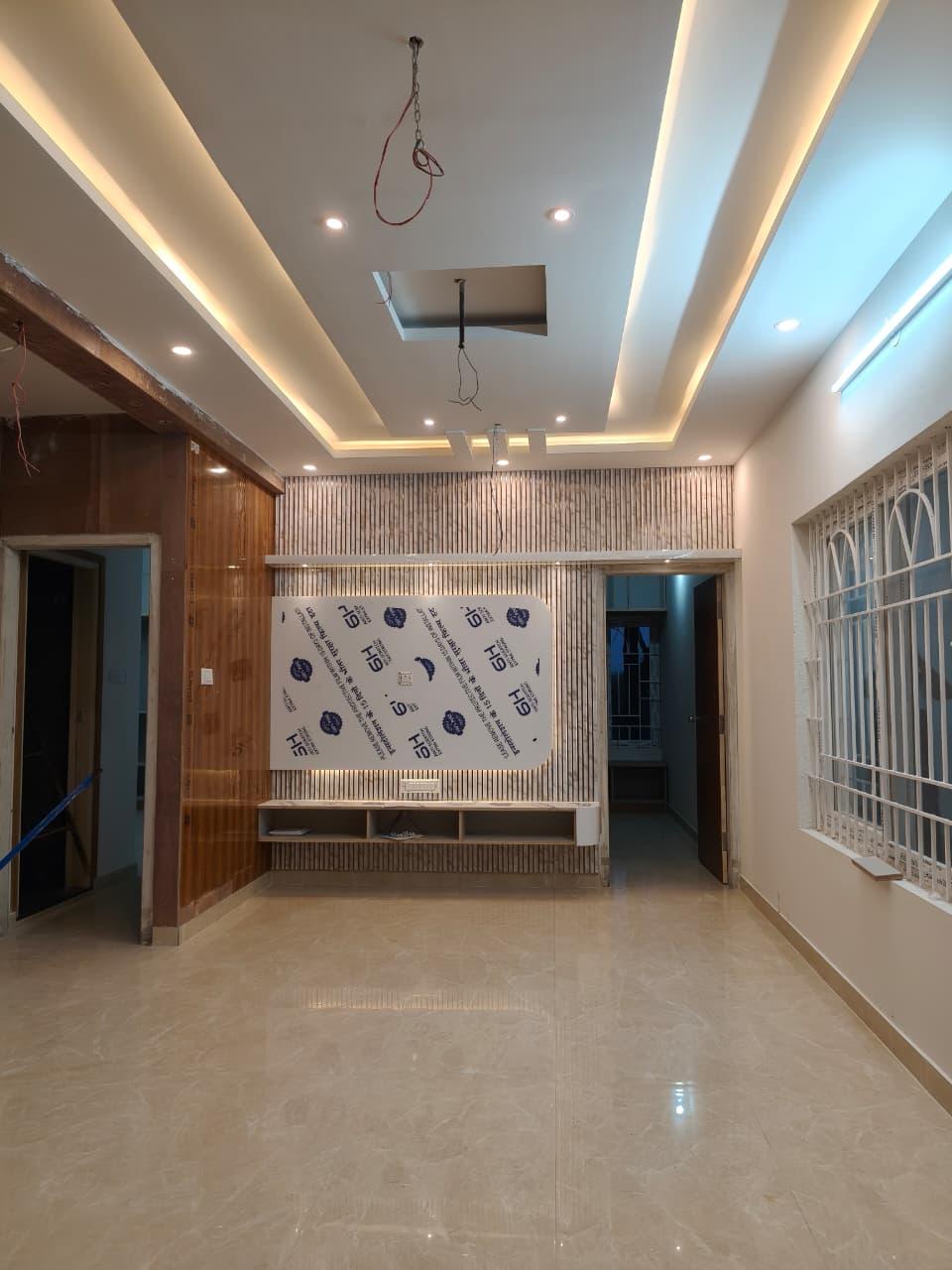 A flat under finishing: a false ceiling with recessed cove lighting above fluted wall panelling, with floor protection still down and cables hanging for the lighting connection.